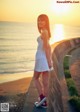 A woman in a white dress standing on a wall by the ocean.