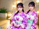 Two young women in kimonos sitting on a wooden bench.