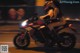 A woman riding a motorcycle on a city street at night.