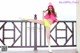 A woman in a pink top and yellow shorts posing on a balcony.