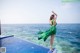 A woman in a green dress standing on the edge of a swimming pool.